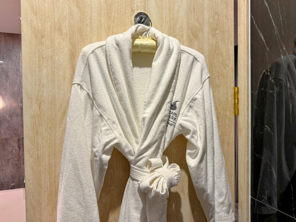 木目調のクローゼット扉に掛けられた、清潔な白いバスローブ。左胸にホテルのロゴ刺繍が入っている。