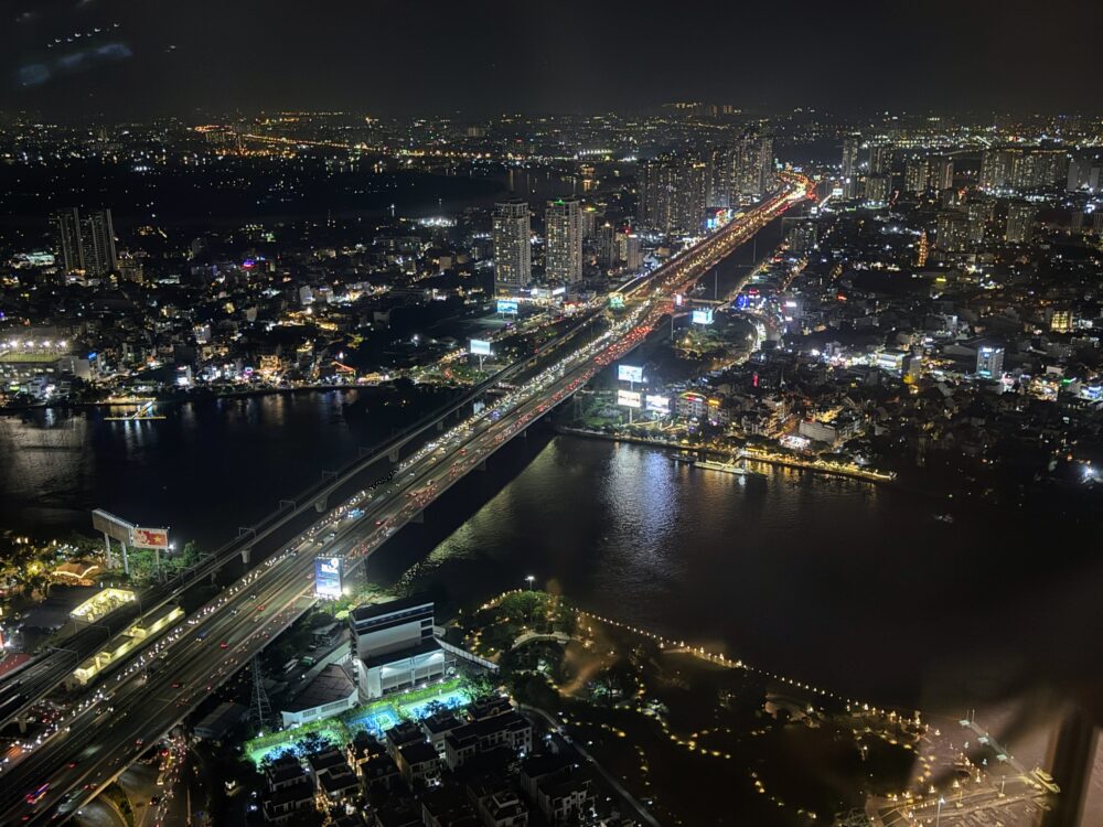 超高層階の窓から広がるホーチミン市内のパノラマ夜景。無数の街灯りと、暗いサイゴン川のコントラストが美しい。