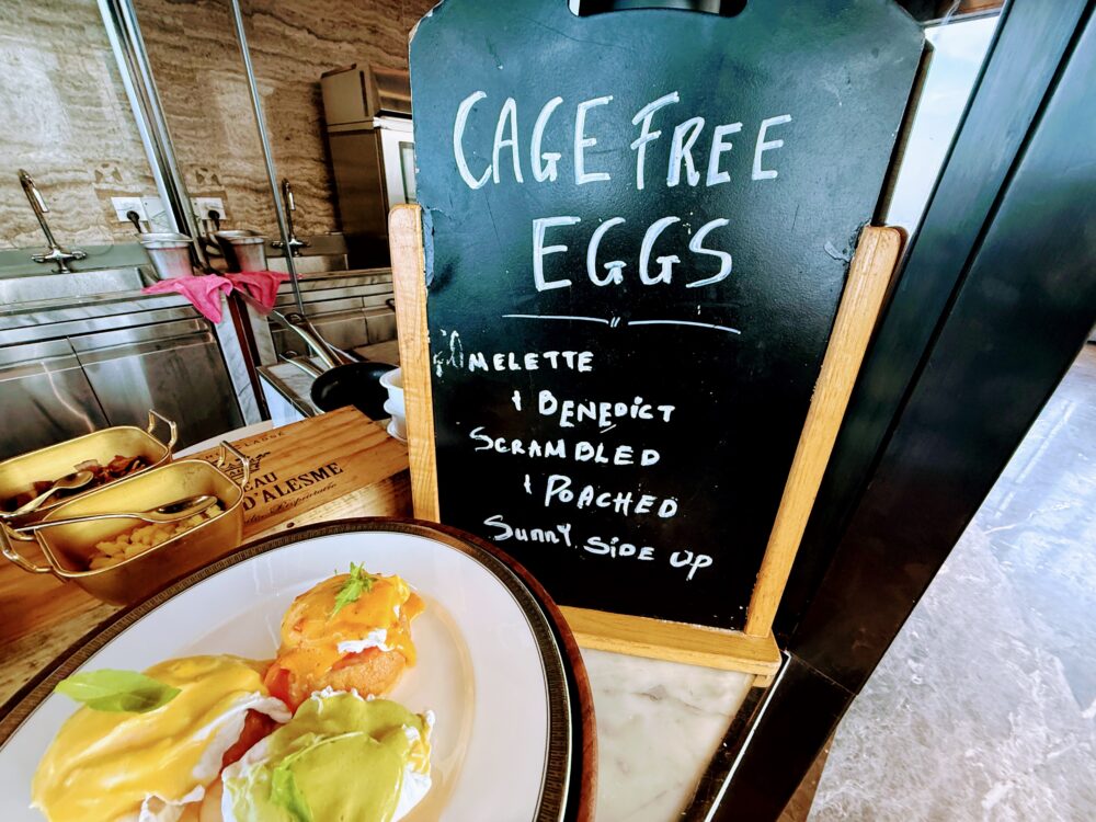 「CAGE FREE EGGS」と書かれた黒板メニュー。オムレツ、ベネディクト、スクランブルなどのオーダーが可能。手前にはエッグベネディクトの皿がある。