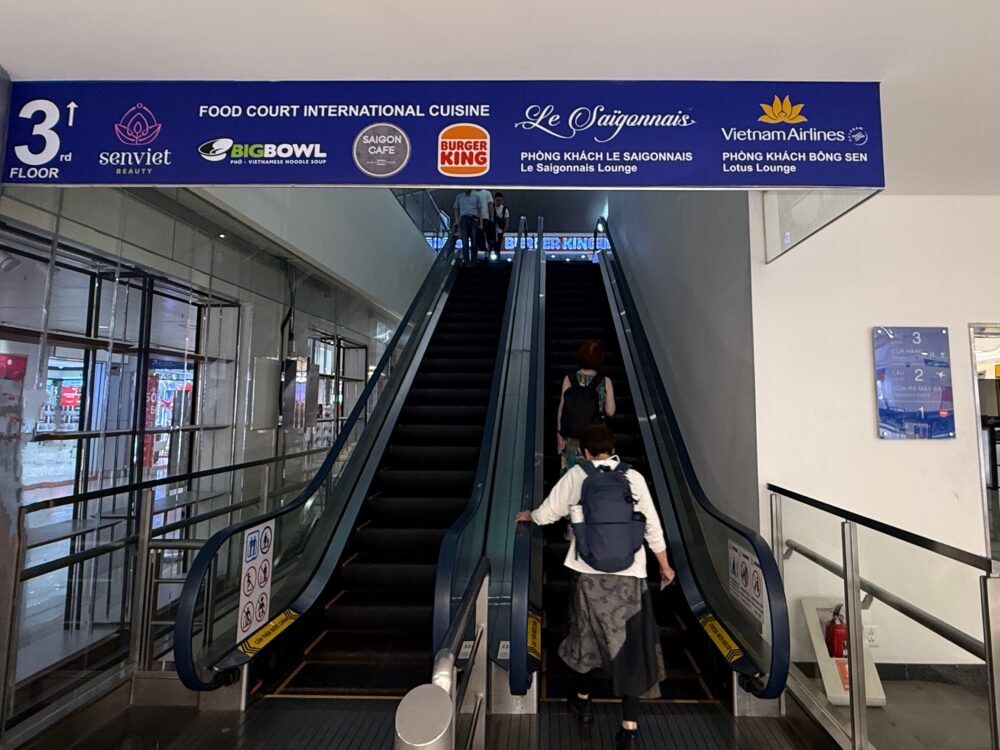 3階のロータスラウンジ1へ向かうエスカレーター。頭上の青い看板にラウンジの表示がある。