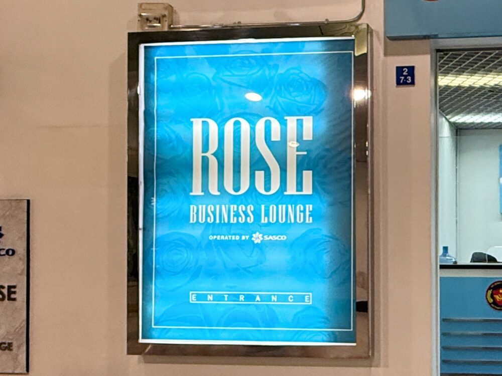 ホーチミン・タンソンニャット国際空港国際線ターミナルにある「ROSE BUSINESS LOUNGE（ローズビジネスラウンジ）」の入り口看板。青い背景に白い大きな文字でラウンジ名が発光しており、下部に「OPERATED BY SASCO」と記載されている。