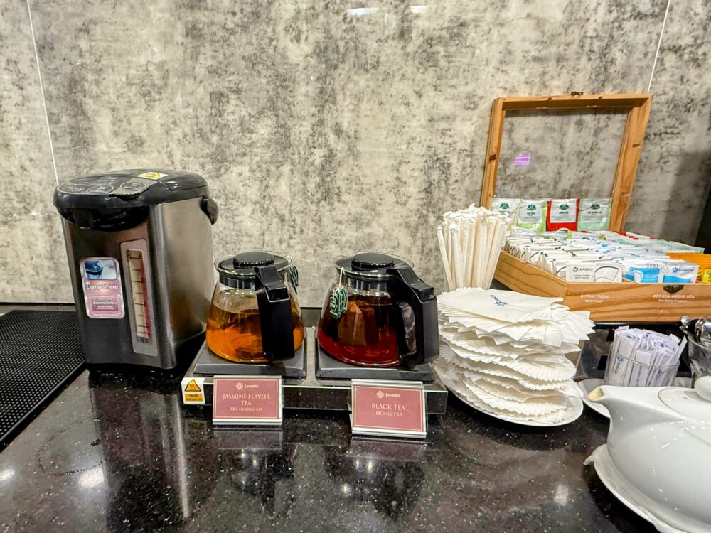 ウォーマーの上に置かれた2つのガラス製ティーポット。左側は「JASMINE FLAVOR TEA（ジャスミン茶）」、右側は「BLACK TEA（紅茶）」の札が付いている。左には給湯ポット、右奥にはティーバッグが入った木箱がある。