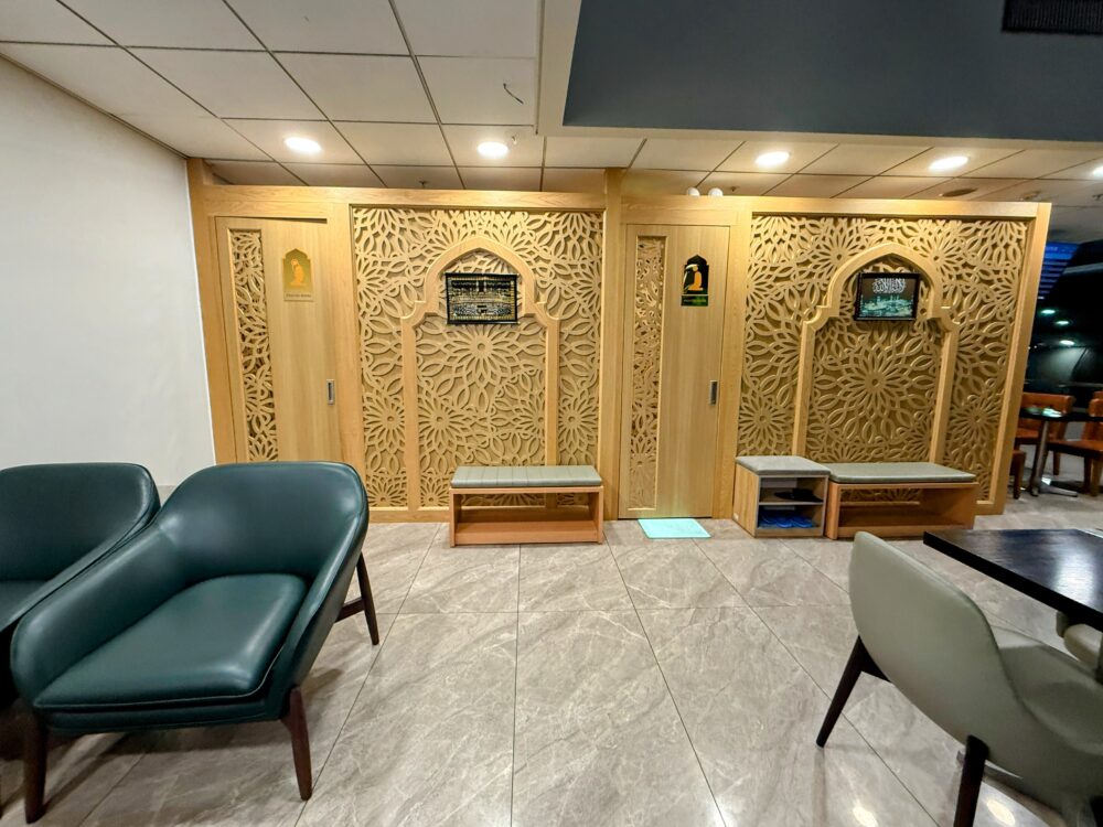 ラウンジ奥にある礼拝室（Prayer Room）の入り口。壁面は美しい木製の幾何学模様で装飾されている。左が女性用、右が男性用の入り口となっており、手前には靴を脱ぐためのベンチと棚、休憩用のソファが設置されている。