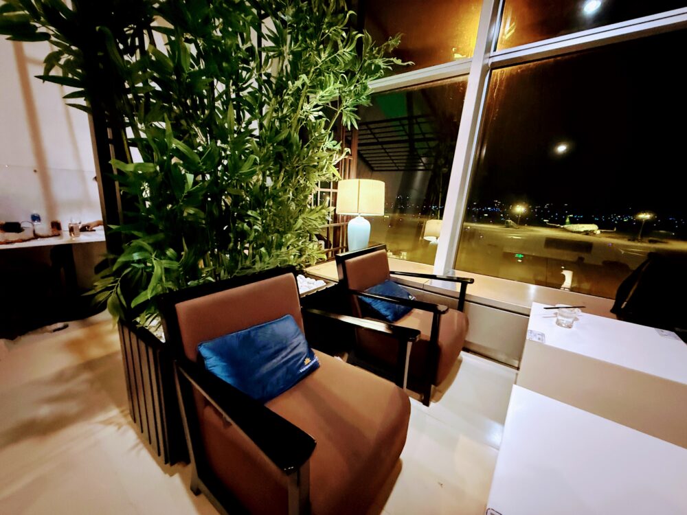 ロータスラウンジ1のラウンジ内観。クッション付きのゆったりしたソファ席と目隠しの観葉植物、窓の外には夜の空港の景色。