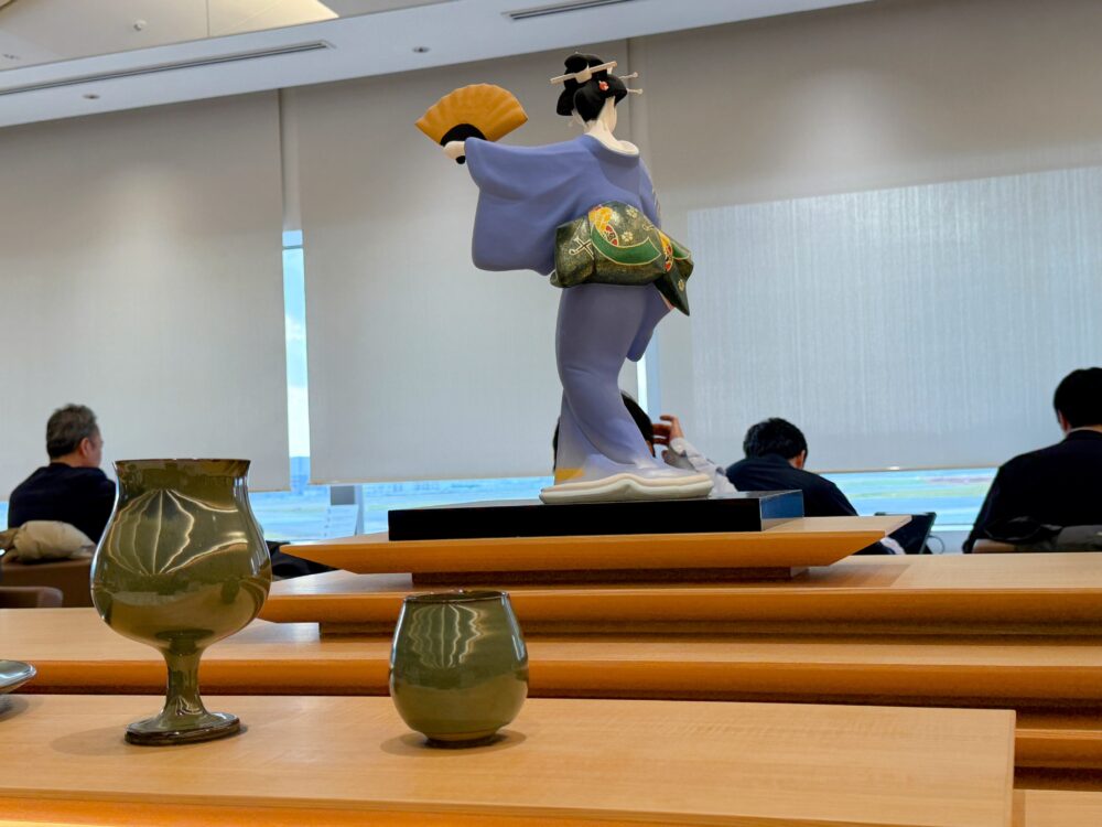 ラウンジ内に展示されている博多人形の後ろ姿と、福岡の伝統工芸品である緑色の高取焼（陶器）。