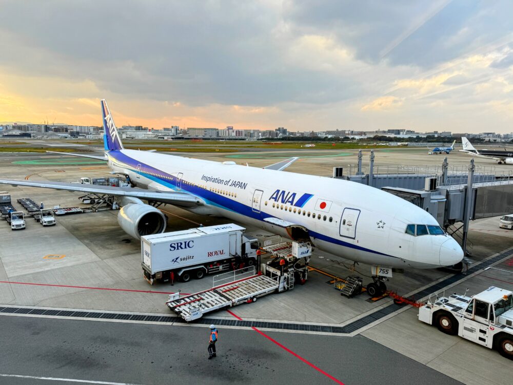 福岡空港ANAスイートラウンジの窓から見えるANAの大型旅客機（ボーイング777）。夕暮れの駐機場で荷物の積み込み作業が行われている様子。