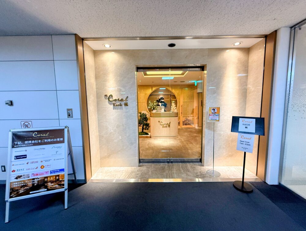コーラルラウンジ楓（かえで）の正面入口。高級感のある大理石調の壁面にゴールドのロゴが輝き、右手には営業時間（7:00-22:00）を示す案内板がある。