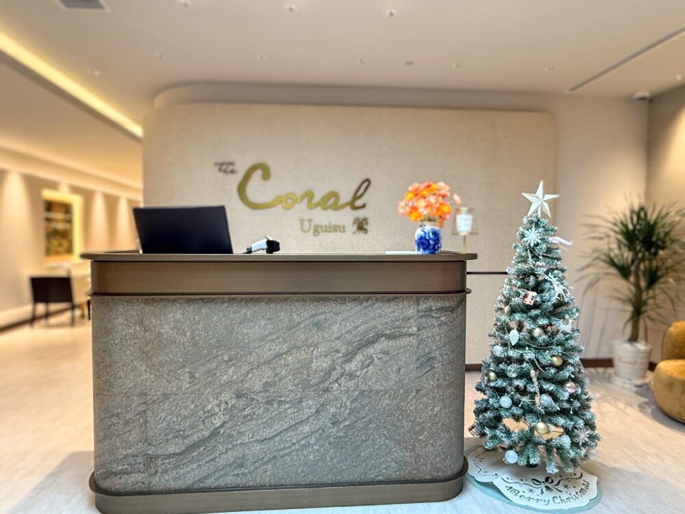 中部国際空港コーラルラウンジ鶯（うぐいす）の受付カウンター。「The Coral Uguisu」のロゴとクリスマスツリーが飾られた石造りのモダンなエントランス。