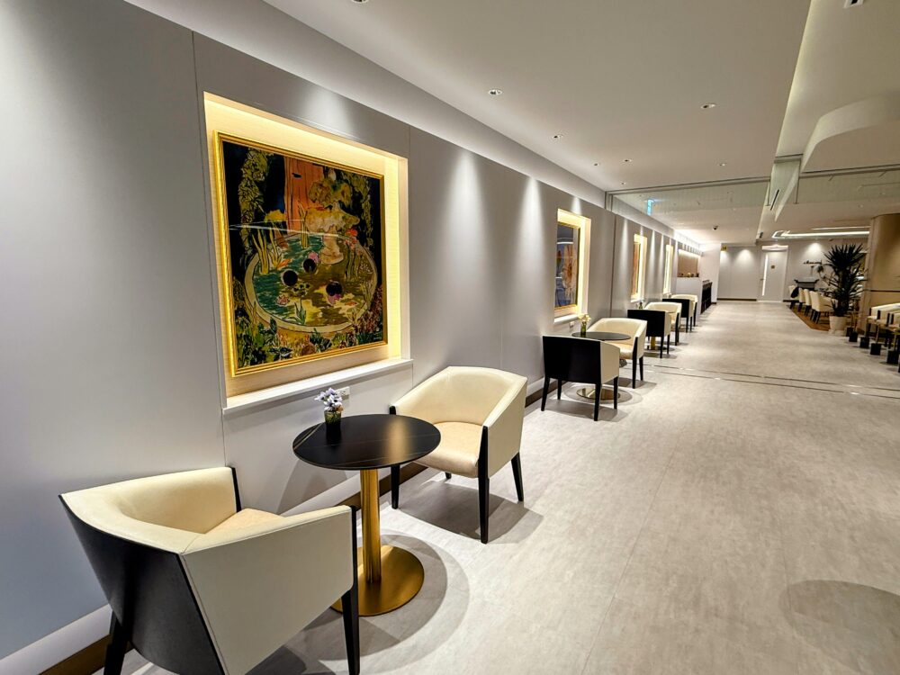 ラウンジ内の通路。壁にはアート作品が飾られ、ダウンライトで照らされた高級感のある白い床の廊下。