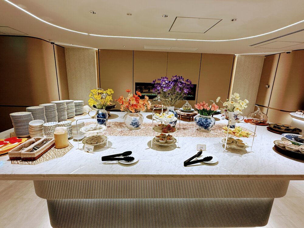 白大理石の清潔感あるビュッフェカウンター。色鮮やかな造花が飾られ、取り皿や小鉢料理が整然と並べられている。