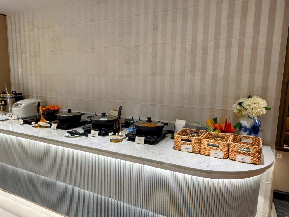 温かい料理が提供されているホットミールコーナー。IHヒーターの上にスープやカレーが入った黒い鍋が並び、炊飯器も用意されている。