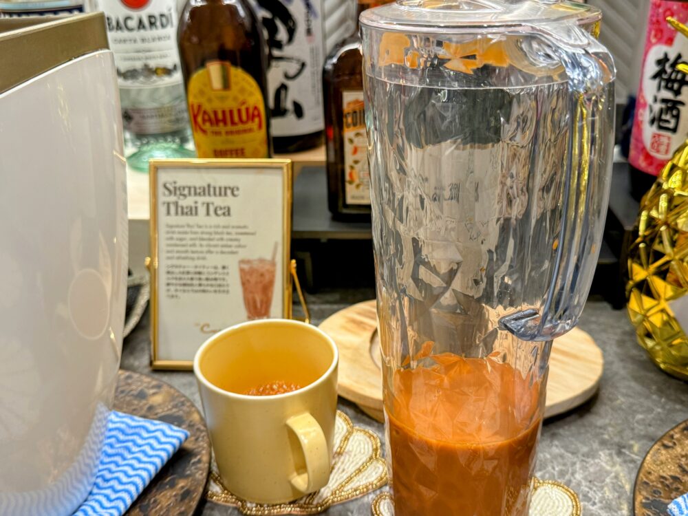 コーラルラウンジ名物の「シグネチャー・タイティー」。ピッチャーに入った鮮やかなオレンジ色のアイスミルクティーと、紹介ポップ。