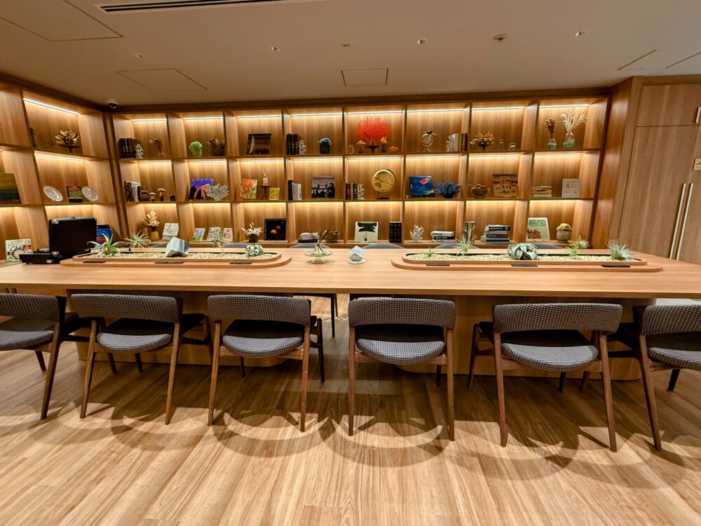 中央に観葉植物が配置された大きな木製のロングテーブル席。グループ利用やミーティングにも適した開放的なデザイン。