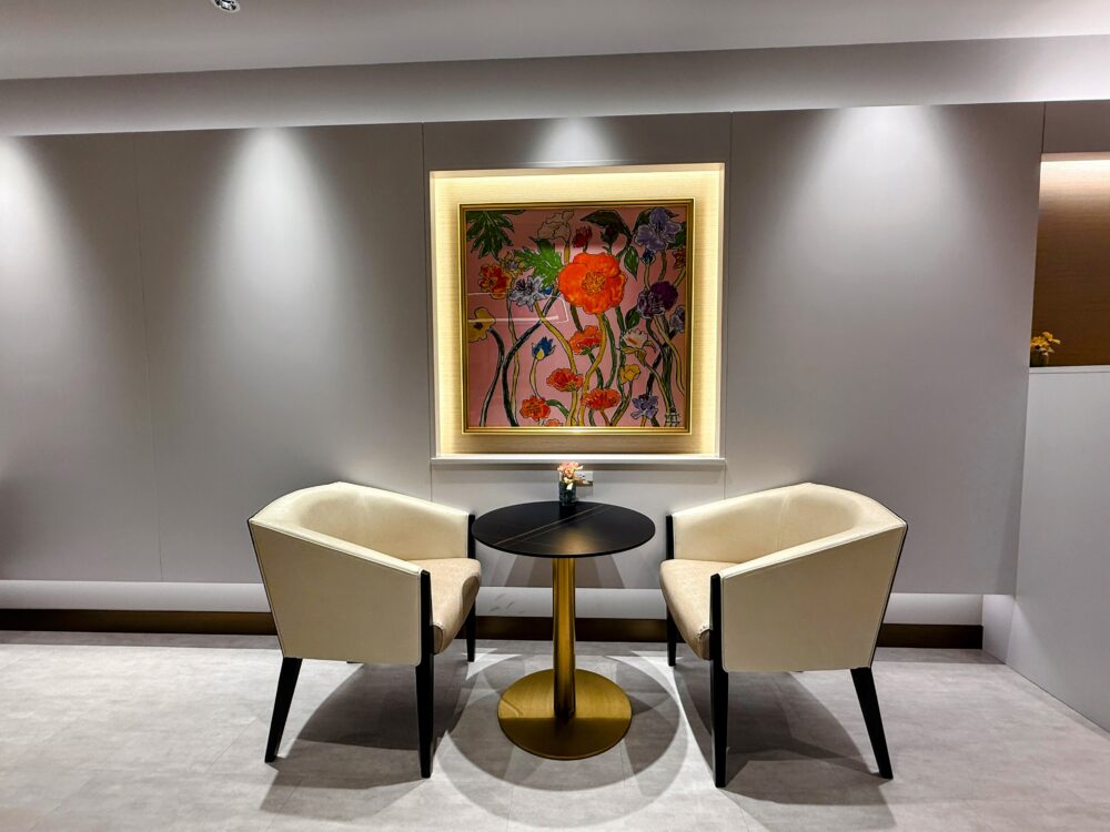 壁に鮮やかな花の絵画が飾られた、2人掛けのテーブル席。白いレザー調の椅子が配置されたエレガントな空間。