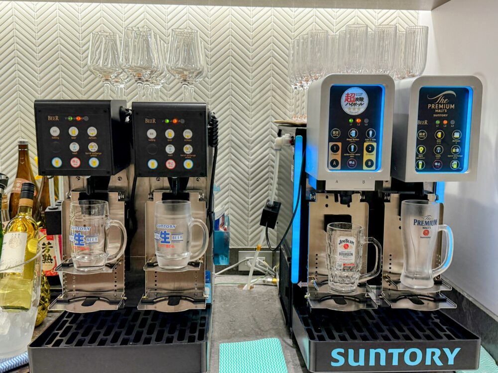 全自動ビールサーバーとハイボールサーバー。サントリー・ザ・プレミアム・モルツとジムビームのロゴが光り、冷えたジョッキが用意されている。
