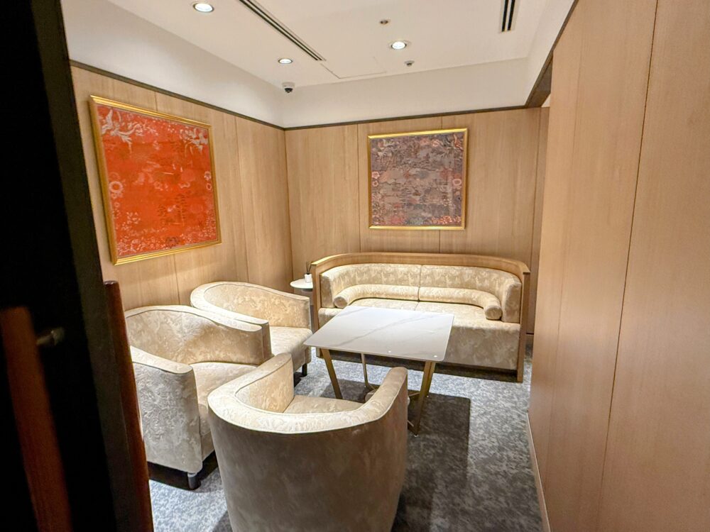 コーラルラウンジ楓にある完全個室のVIPルーム。壁には赤い抽象的なアートが飾られ、高級感のある白い一人掛けソファーとソファーベンチが対面で配置されている。