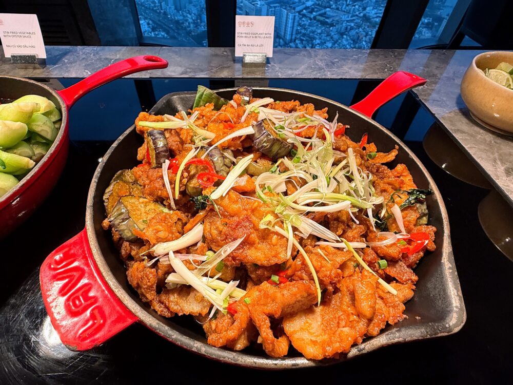 赤い鉄製スキレット(LAVA社製)に盛られた、茄子と豚バラ肉の炒め物(ロットの葉風味)。たっぷりの白髪ネギと唐辛子がトッピングされている。