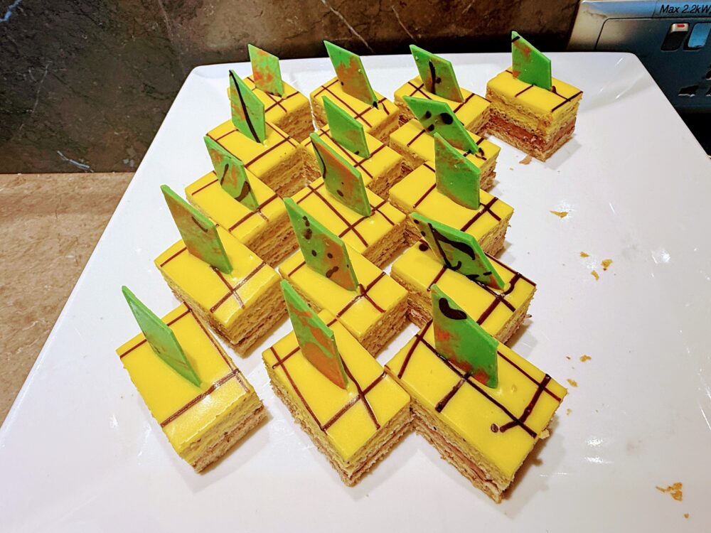 鮮やかな黄色のスポンジに緑のチョコレートが飾られた一口サイズのケーキ。