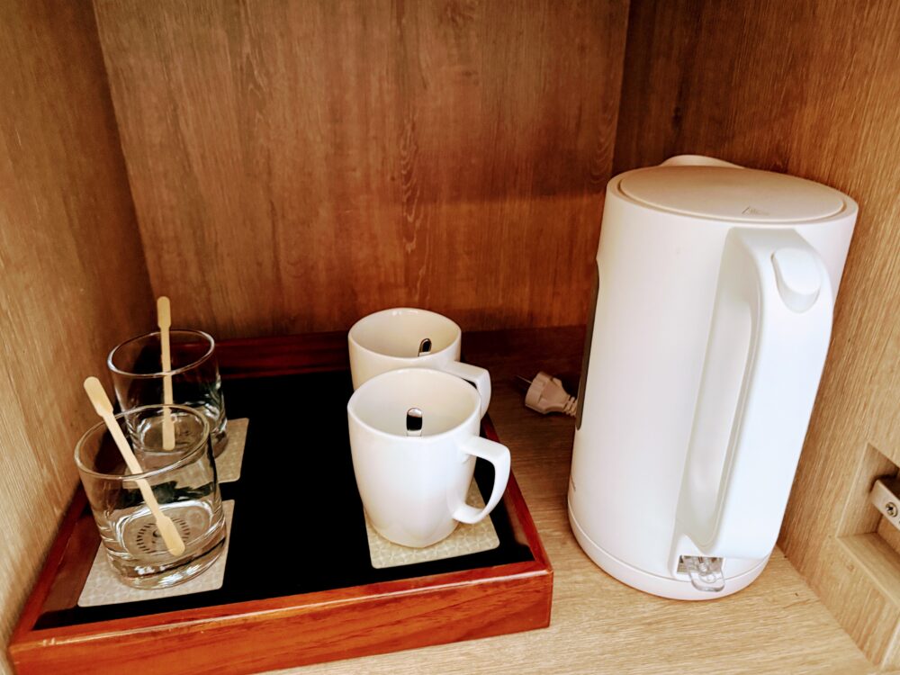 木製のキャビネット内に収納された白い電気ケトル、マグカップ、グラスのセット。