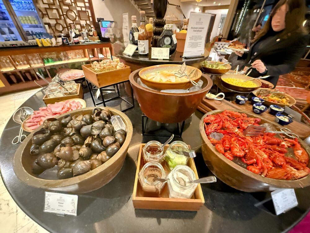 カクテルタイムのビュッフェカウンター。手前にエスカルゴ、奥にザリガニやサラダなど豪華な料理が並んでいる様子。