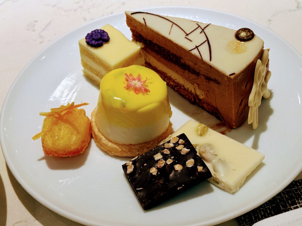 皿に美しく盛り付けられた本日のデザート(チョコレートヘーゼルナッツケーキ、パッションフルーツムース、ホワイトオペラ、割りチョコレートなど)。