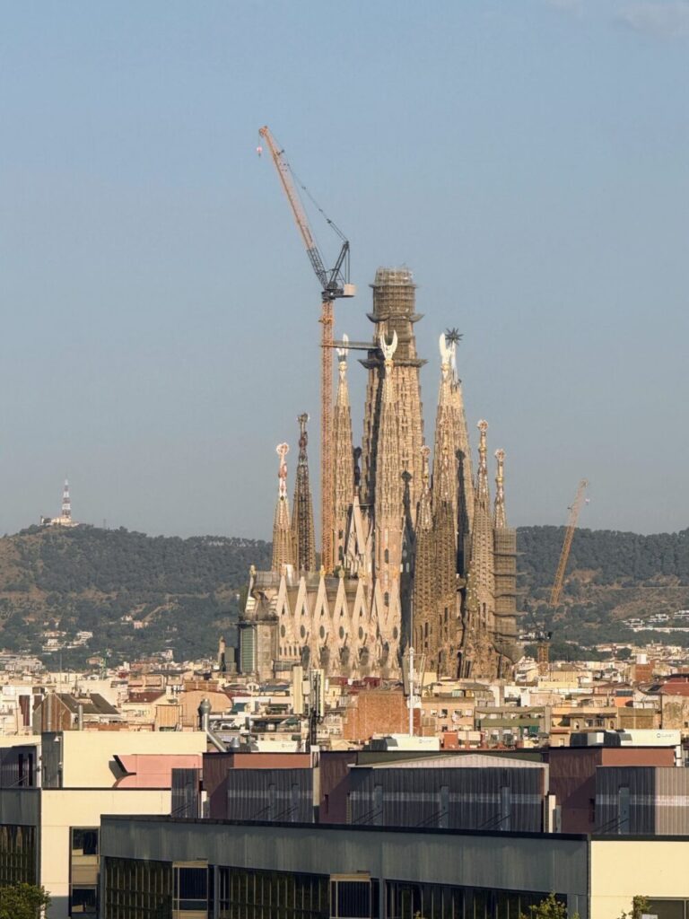 ホテルのエレベーターホールから正面に見える、青空の下のサグラダ・ファミリアと建設用クレーン。