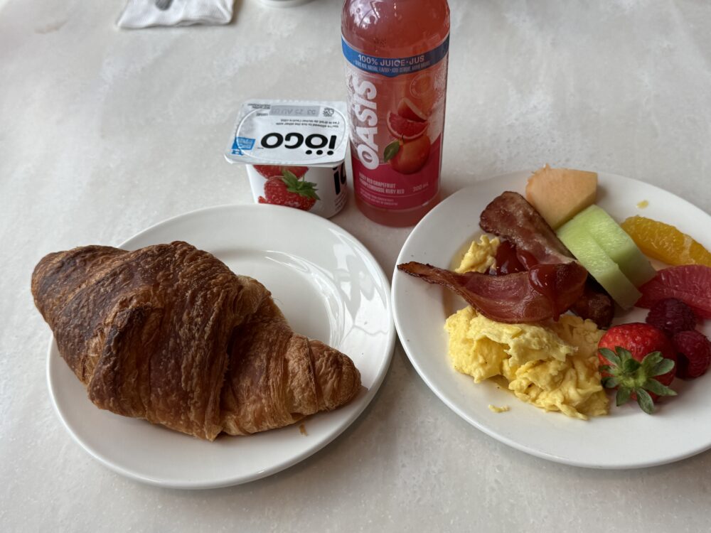 ラウンジで盛り付けた朝食プレート。大きなクロワッサン、スクランブルエッグ、ベーコン、フルーツ、ヨーグルト、ジュースのセット。