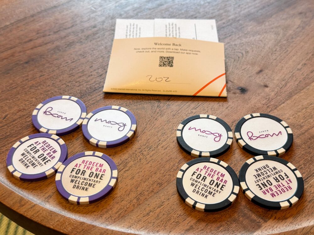 テーブルに置かれたルームキー(202号室)と、ウェルカムドリンク用のポーカーチップ型コイン(紫4枚、黒4枚の計8枚)。