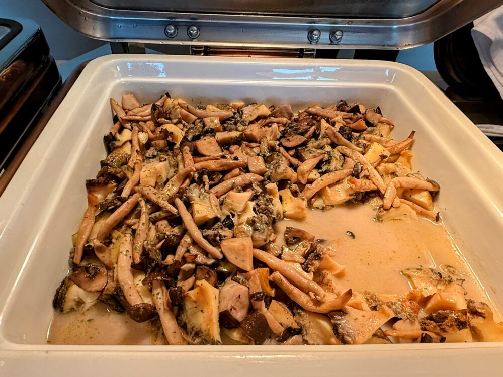 チェーフィングディッシュに盛られた鮑と季節の茸のハーブバターソース。しめじ・ポルチーニなど複数種の茸と鮑がハーブバターソースとともに煮込まれている。