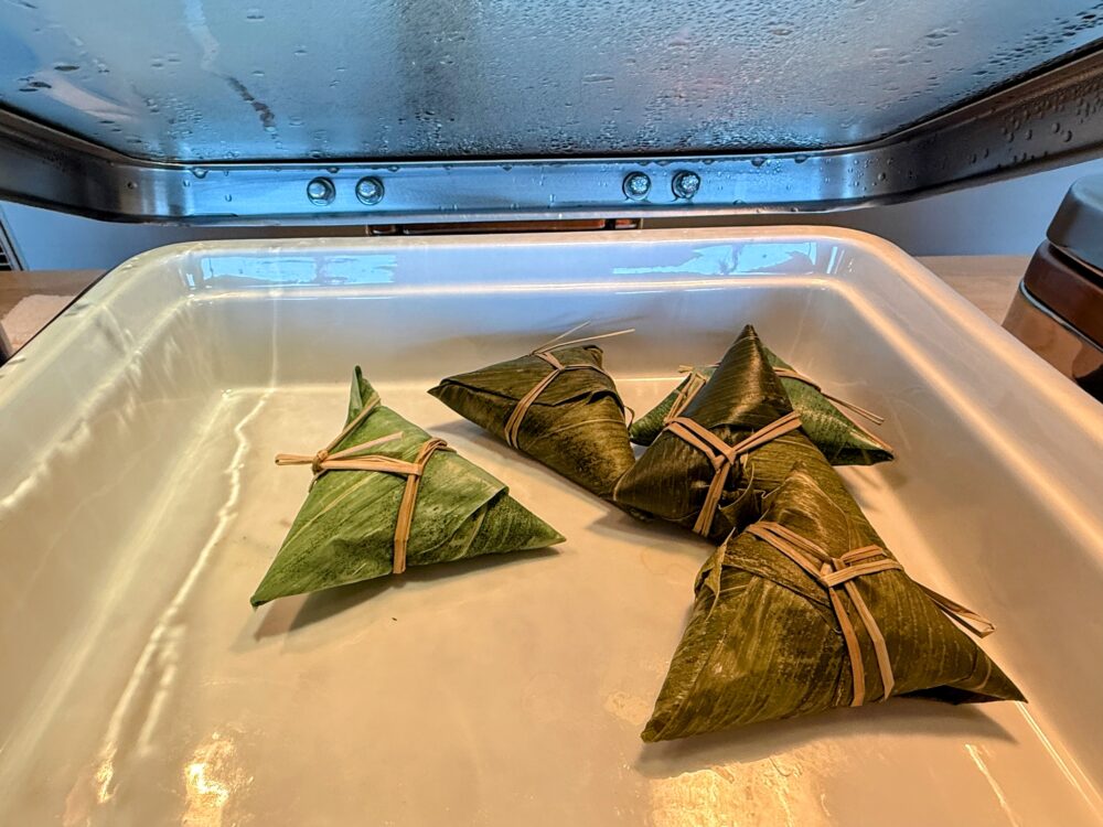 大阪ステーションホテル スペシャリティサロンの朝食ビュッフェに並ぶ中華ちまき。竹の葉で三角形に包まれたちまきが4個、白いトレイに盛られている。