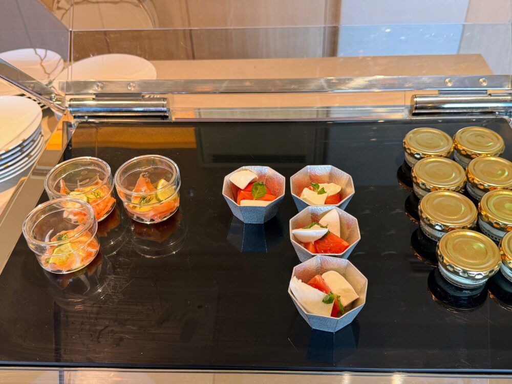 大阪ステーションホテル スペシャリティサロンの朝食ビュッフェに並ぶ冷菜コーナー。スモークサーモンのマリネとトマト&モッツァレラ、キャビアの瓶詰めが黒いカウンターに並ぶ。