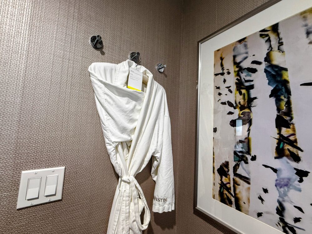 壁のフックに掛けられた白いワッフル地のバスローブ。袖口に「WESTIN」のロゴ刺繍が見える。