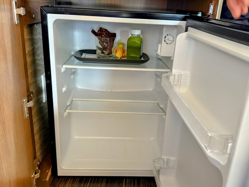 冷蔵庫の中に用意されたウェルカムアメニティ。グラスに入ったチョコレート、フルーツ串、ボトルのグリーンスムージーが冷やされている。