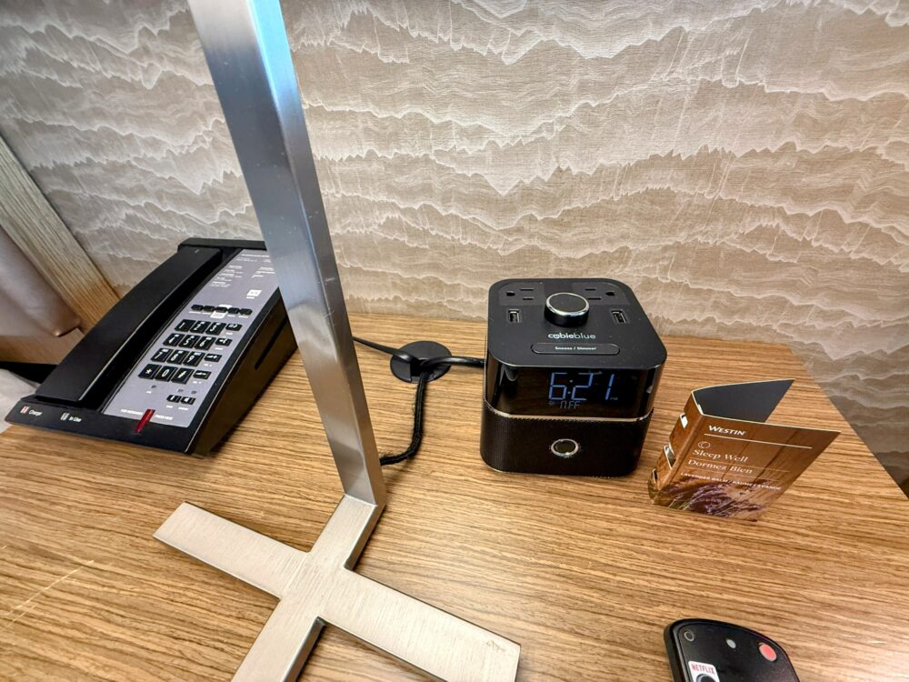 ベッドサイドテーブルの上。黒い多機能時計(cubieblue)、電話機、そして「Sleep Well」と書かれたラベンダーバームのアメニティ。