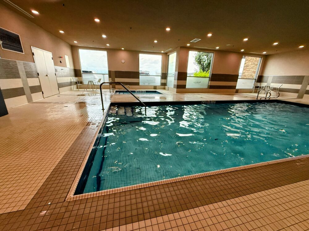 大きな屋内スイミングプール。窓から自然光が差し込み、プールサイドには椅子とテーブルが設置されている。