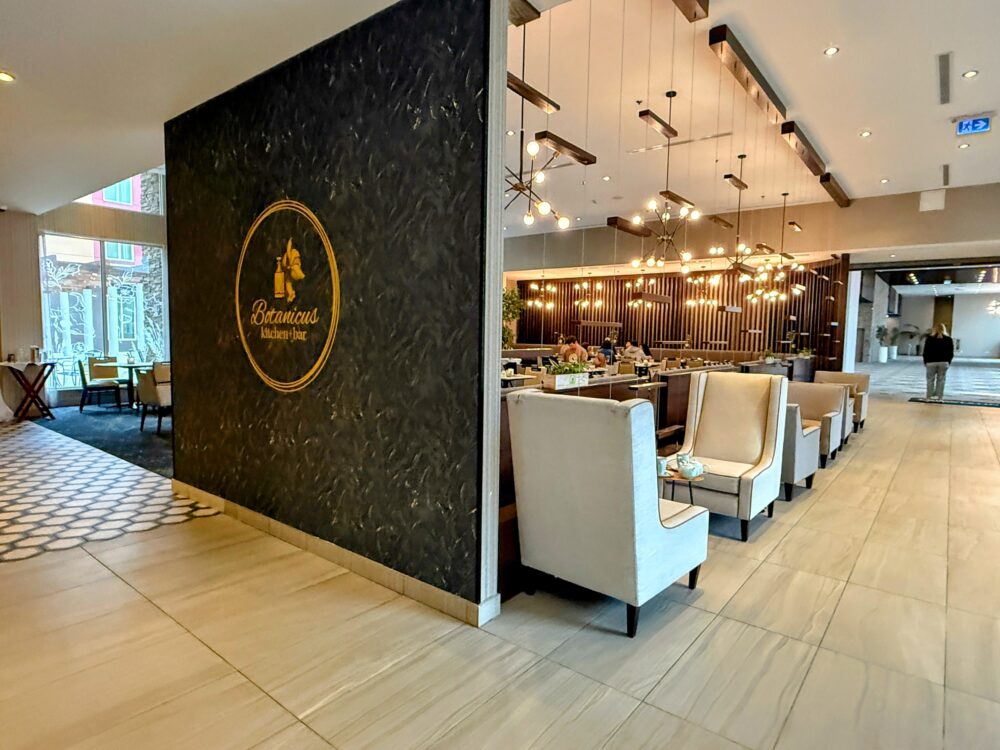 レストラン「Botanicus Kitchen + Bar」の入り口。黒い壁にゴールドのロゴと、手前にはハイバックのラウンジチェア。