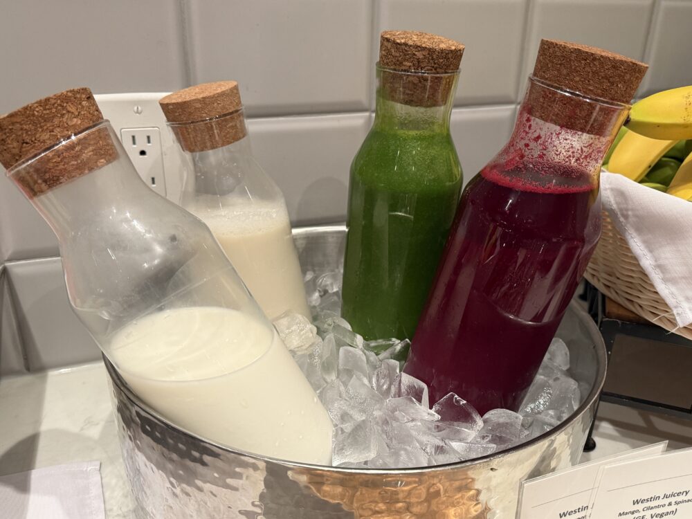 氷を入れたバケツで冷やされているボトル入りスムージー。緑(野菜)、赤(ビーツ)、白(ミルク系)の3種類。