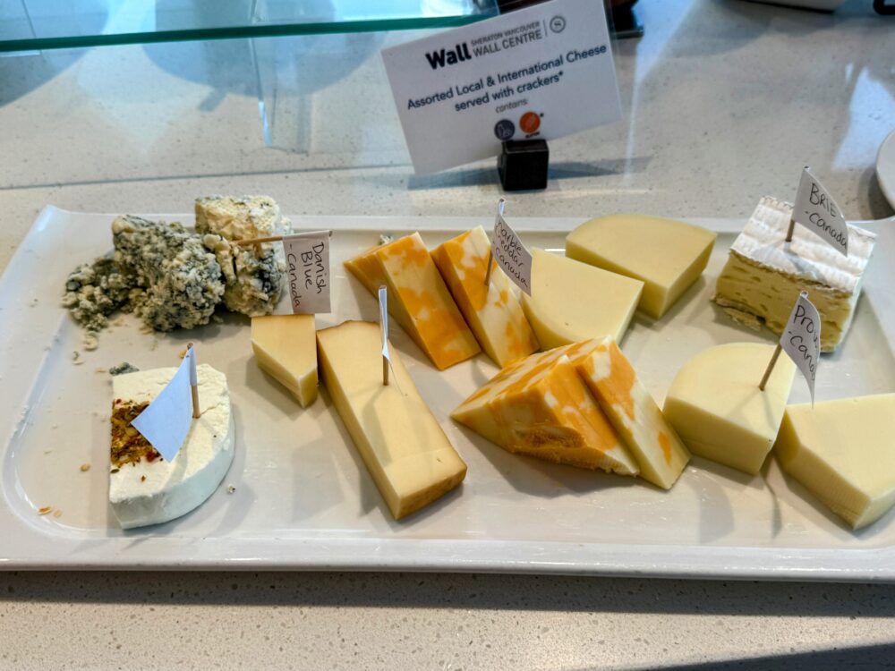 「Assorted Local & International Cheese」のプレート。ブリー、ブルーチーズ、チェダーなど数種類のチーズが一口サイズにカットされ、種類ごとのタグが付けられている。