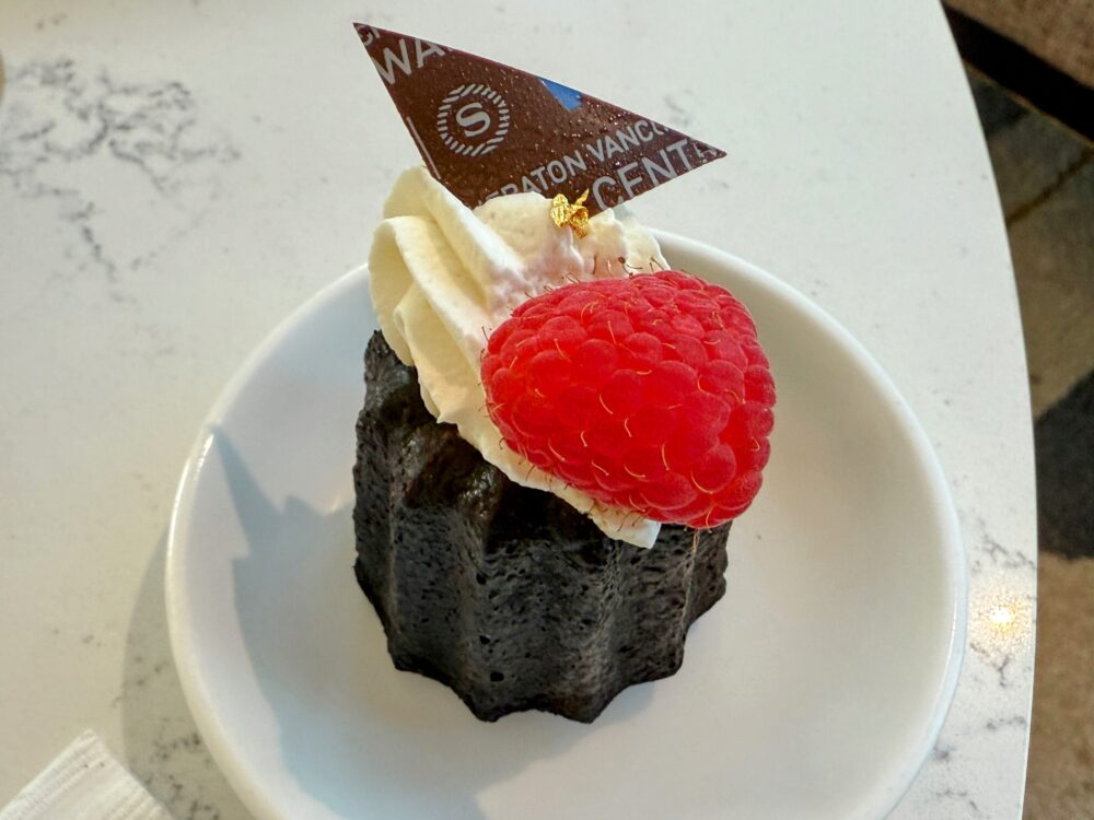 美しくデコレーションされたカヌレ。カヌレの上にはホイップクリーム、赤いラズベリー、金箔、そしてシェラトンのロゴが入った三角形のチョコレートが飾られている。