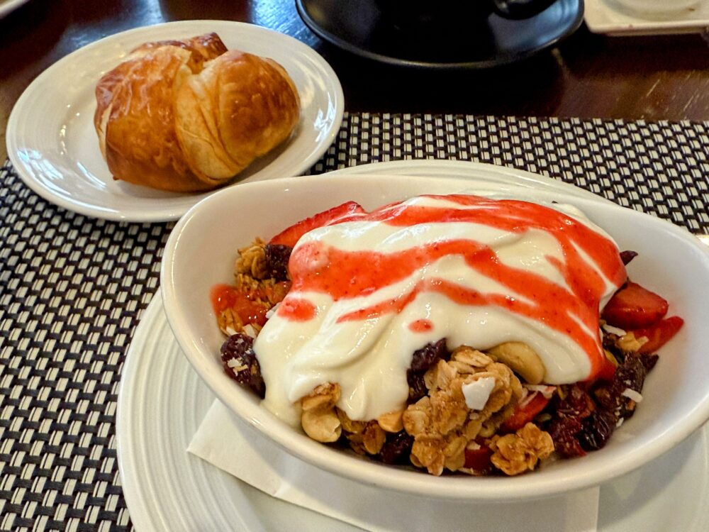 ベリーパフェとクロワッサンの朝食セット。ヨーグルトに赤いベリーソースとグラノーラがたっぷりかかっている。