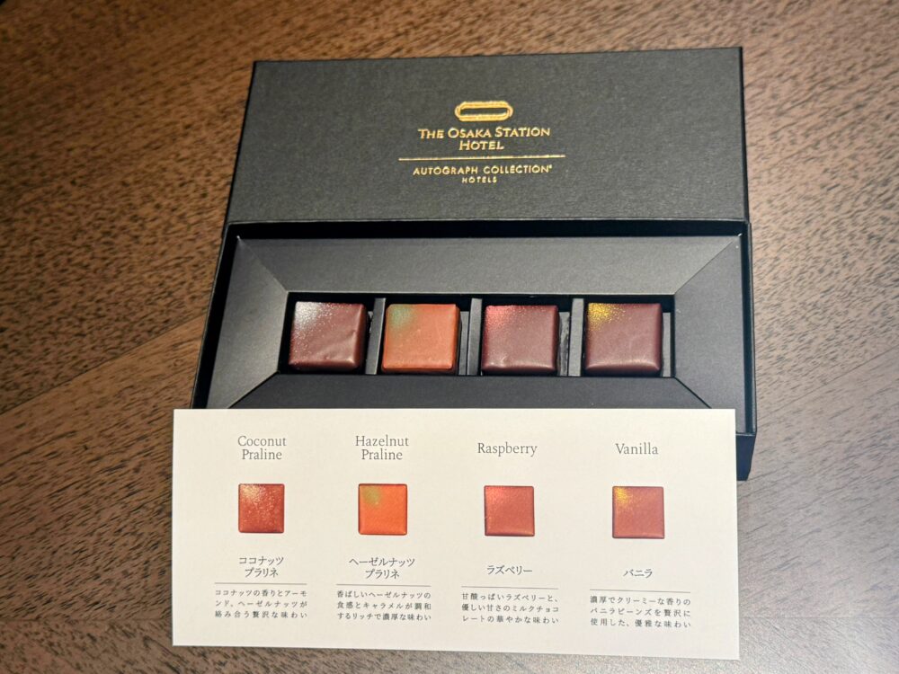 ホテルのロゴが入った黒い箱に入った4種類のウェルカムチョコレート。下にはそれぞれの味(ココナッツ、ヘーゼルナッツ、ラズベリー、バニラ)の説明書きが添えられている。