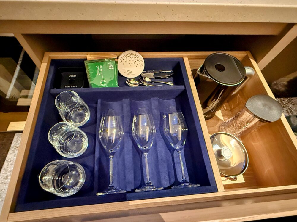 客室の引き出しに収納されたカフェグッズ。グラス類、緑茶のティーバッグ、黒い電気ケトル、ガラスのティーポットなどが綺麗に整頓されている。