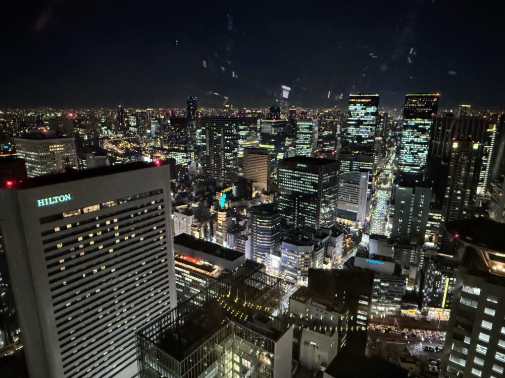 大阪ステーションホテルの客室から見下ろす大阪の美しい夜景。左手には「HILTON」のロゴが光るビルがあり、奥まで光り輝く都会の街並みが続いている。