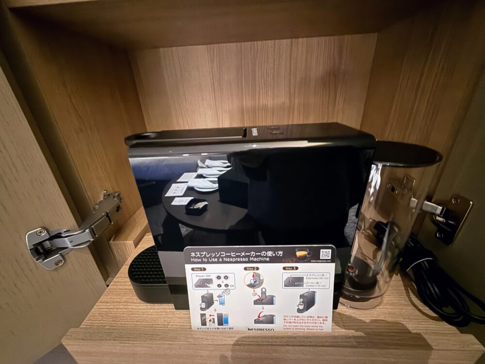 キャビネット下段にある黒いネスプレッソのコーヒーメーカーと使い方の説明書。