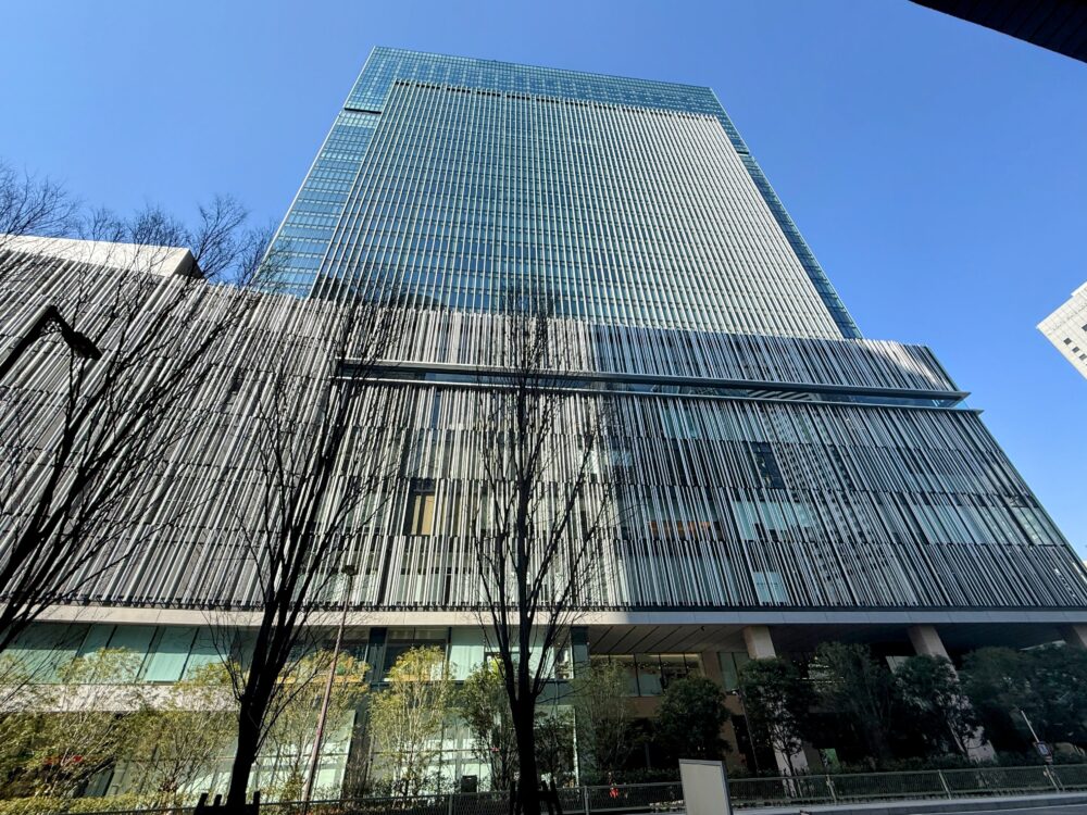 雲一つない青空にそびえ立つ、大阪ステーションホテルが入る「JPタワー大阪」の外観写真。全面ガラス張りの近代的な超高層ビルで、下層階にはスタイリッシュな縦ラインのデザインが施されている。
