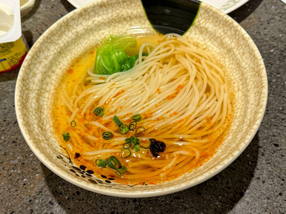 No.71ラウンジLIVEキッチンで仕上げた麺料理。ひび割れ模様の白い丼に細麺が盛られ、赤みがかったスープにねぎが散らされている。