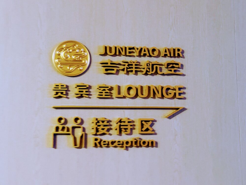 上海浦東国際空港No.72吉祥航空ラウンジの壁面サイン。金色の立体文字で「JUNEYAO AIR 吉祥航空 貴賓室LOUNGE」と表記され、レセプション(接待区)への矢印が右方向に示されている。