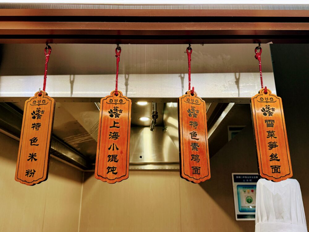 No.72ラウンジLIVEキッチンの木製メニュー札。「特色米粉」「上海小馄饨(ワンタン)」「特色素鶏麺」「雪菜笋丝麺」の4種が天井から吊り下げられている。