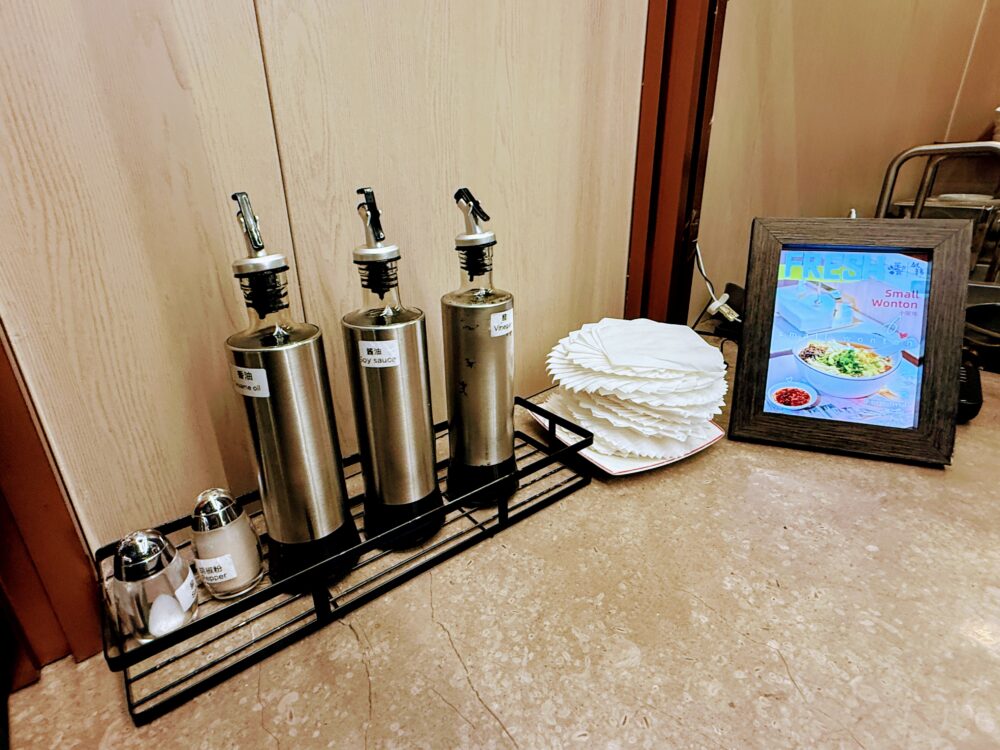 No.72ラウンジLIVEキッチンカウンターの調味料セット。ごま油・醤油・酢・胡椒が並び、手作りワンタンの皮が積まれている。右にSmall Wontonのメニューパネルが見える、