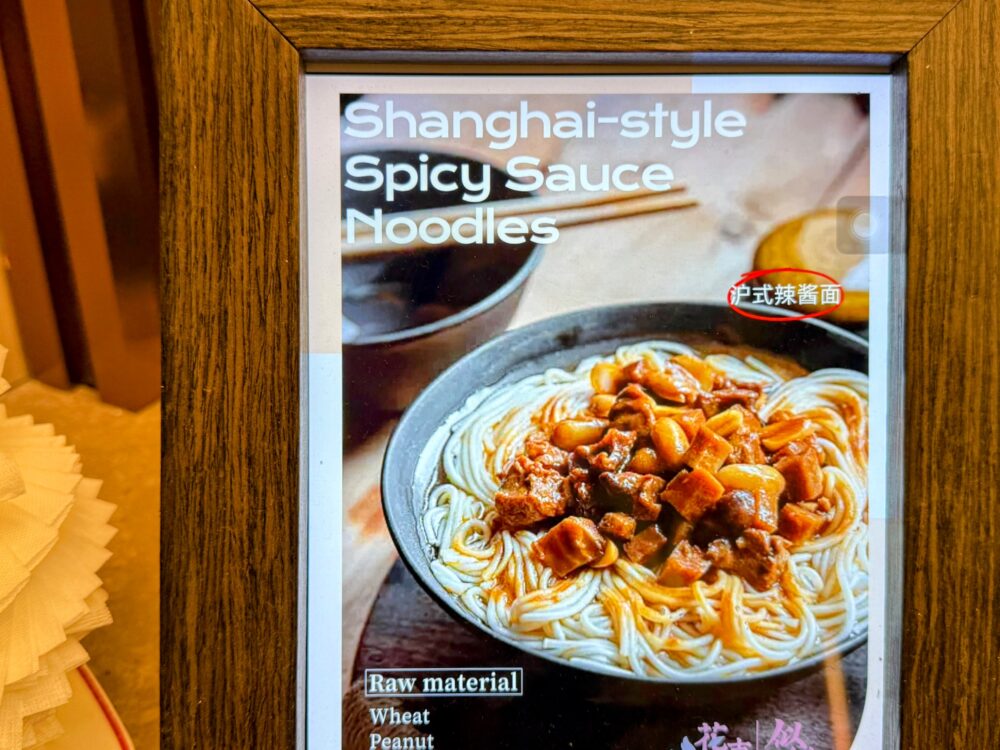 No.72ラウンジLIVEキッチンのメニュー写真。「Shanghai-style Spicy Sauce Noodles(沪式辣醤麺)」の完成イメージが額縁に入って展示されている。